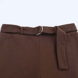 Detail of dark brown trousers featuring a knit fabric waist with silver double D-ring belt