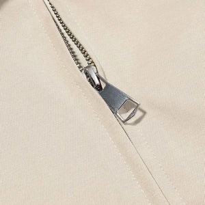 Detailed macro view of silver metal zipper on light beige twill fabric garment jacket