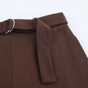 Detail of dark brown trousers waist with textured fabric and belt with silver D-ring
