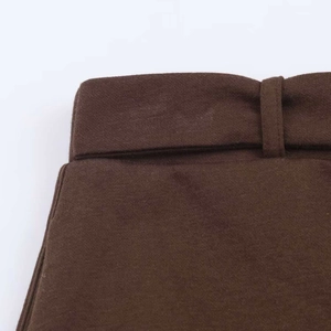 Detailed macro view of the waist stitching and belt loops on brown tailored trousers