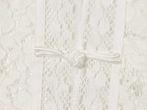 Close-up of white lace fabric with floral patterns and a traditional frog button fastener