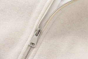 Detailed macro shot of silver metal zipper on soft cream-colored wool bomber jacket