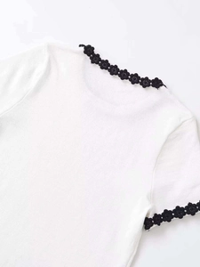 Detail of white knit top featuring black crochet floral lace on collar and sleeves