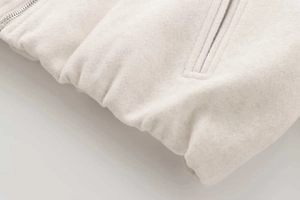 Detailed close-up of cream wool bomber jacket with silver metal zipper and welt pocket