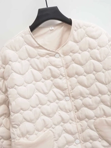 Detail view of heart-quilted puffer jacket in cream with snap buttons and neck size label