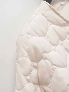 Detailed close-up of beige heart-shaped quilted pattern on soft puffer jacket fabric