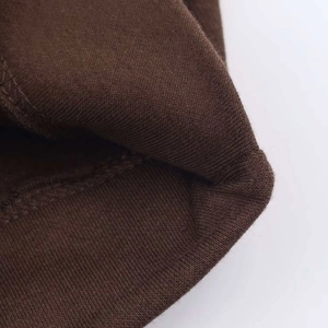 Detailed close-up of dark brown knitted cotton fabric showing double-needle hem stitching