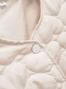 Detailed close-up of heart-shaped quilting and round snap button on cream vest, size S label