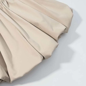 Detail of beige pleated bubble skirt fabric showing textured puffy silhouette design