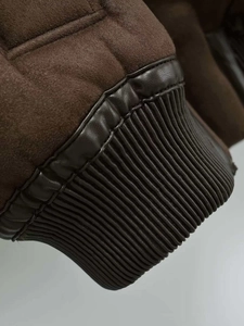 Detailed close-up of dark brown suede jacket showing leather trim and ribbed cuff texture