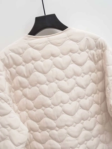 Detailed close-up of heart-shaped quilting patterns on a cream white puffer jacket