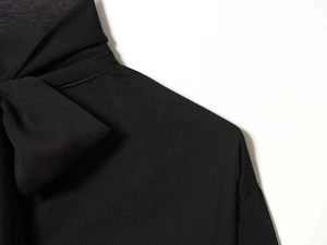 Detail of elegant black pleated shirt featuring a large bow tie on the collar area