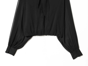 Detail of sheer black pleated shirt with bow neckline and elastic waist hem for women