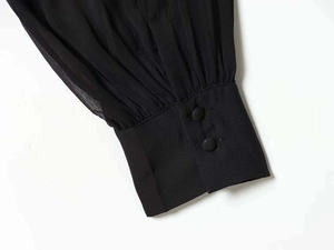 Detail of pleated black chiffon sleeve with two matching fabric-covered buttons on the cuff