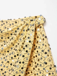 Macro detail of vibrant yellow skirt featuring intricate silver and gold sequin swirls