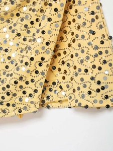 Close-up of yellow mini skirt with intricate silver and black sequin swirls