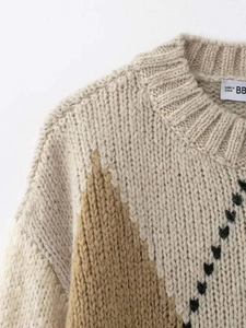 Gros plan sur le col ras du cou côtelé et le pull en tricot géométrique à losanges beige