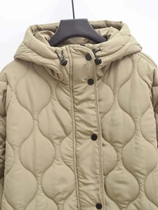 Detail of wave-quilted khaki jacket featuring hooded drawstring and black press studs