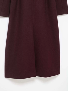 Detail view of the hem and cuffs on a dark burgundy wool coat with fine texture