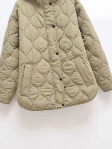 Detail view of wavy quilted texture and black button closure on beige hooded coat