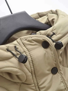Detail view of khaki hooded jacket with snap buttons, black toggles, and wave quilting texture