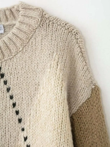 Détail d'un pull en maille beige avec motif cœur noir et col rond côtelé élégant