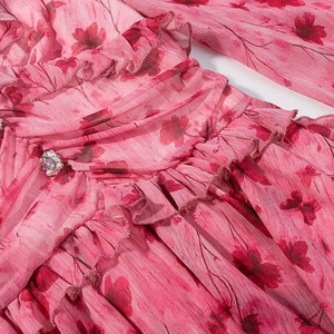 Detail of pink floral dress featuring ruffled chiffon layers and pearl jewel button