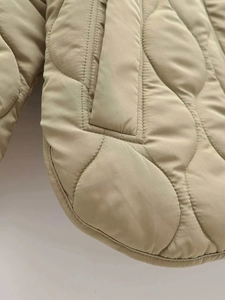 Detail of the wave-quilted beige coat showing textured stitching and windproof fabric