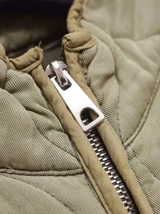 Macro detail of high-quality silver metal zipper on quilted olive green jacket fabric