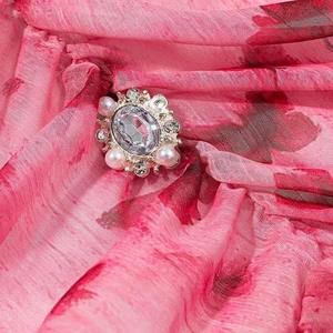 Detail of vintage oval gemstone brooch with white pearls and rhinestones on chiffon dress
