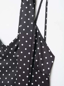 Détail du décolleté en V et des fines bretelles d'une robe noire à pois