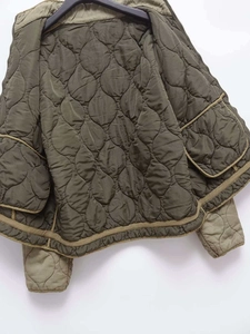 Detail view of olive green quilted jacket with wave stitching and large patch pockets