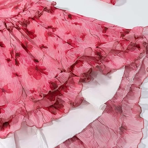 Detailed macro view of multi-layered ruffled hem with red floral print on pink chiffon dress
