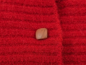 Detail shot of a red mohair knit garment with a textured brown marble button