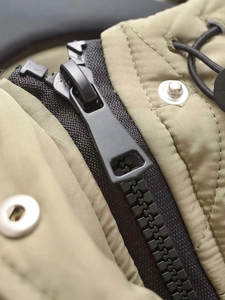 Detailed macro of olive green quilted jacket featuring black resin zipper and metal snap