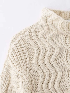 Close-up of cream cable-knit sweater detail showing high neck and intricate texture
