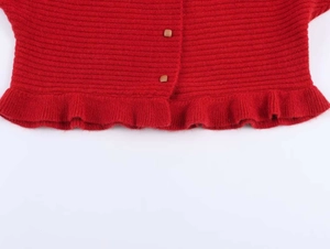 Detail of red ribbed knit top featuring wood-style buttons and ruffled hemline
