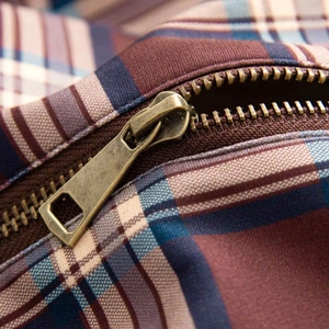Detailed close-up of antique bronze zipper on vintage plaid fabric bomber jacket
