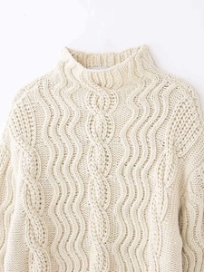 Macro shot of cream cable knit sweater showing textured wave pattern and high neckline