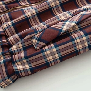 Detailed close-up of retro plaid bomber jacket pocket with brown and navy check pattern