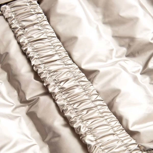 Macro view of metallic champagne quilted fabric with elastic pleat detail and glossy finish