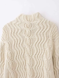Close-up of the cream cable knit turtleneck sweater showing thick braided stitch details
