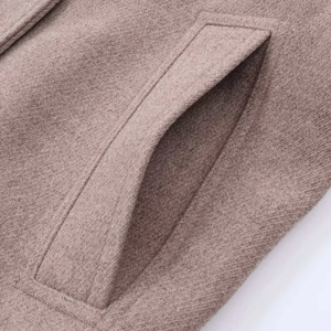 Macro detail of brown wool coat showing woven texture and precise stitching on the pocket