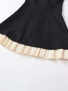Detail of black midi dress showing a cream pleated hem and contrast stitching texture