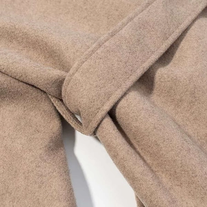 Detailed close-up of the belt loops and soft wool texture on a camel long coat