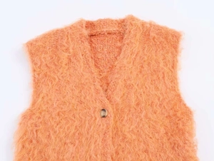 Détail rapproché d'un gilet en tricot peluche orange corail avec col en V et bouton brun