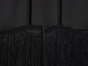 Detail shot of the black textured fabric and long tassel fringe on the halter dress hem