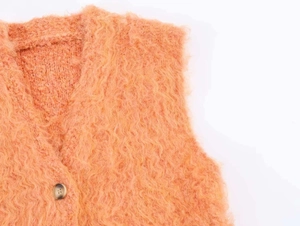 Gros plan du gilet en maille peluche orange montrant la texture douce et le col en V
