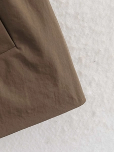 Detail shot of the brown trench coat's woven fabric texture and hemline finish