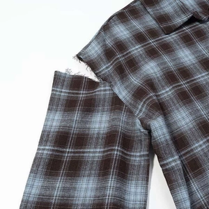 Detail view of deconstructed shoulder cutout with frayed edges on a plaid shirt